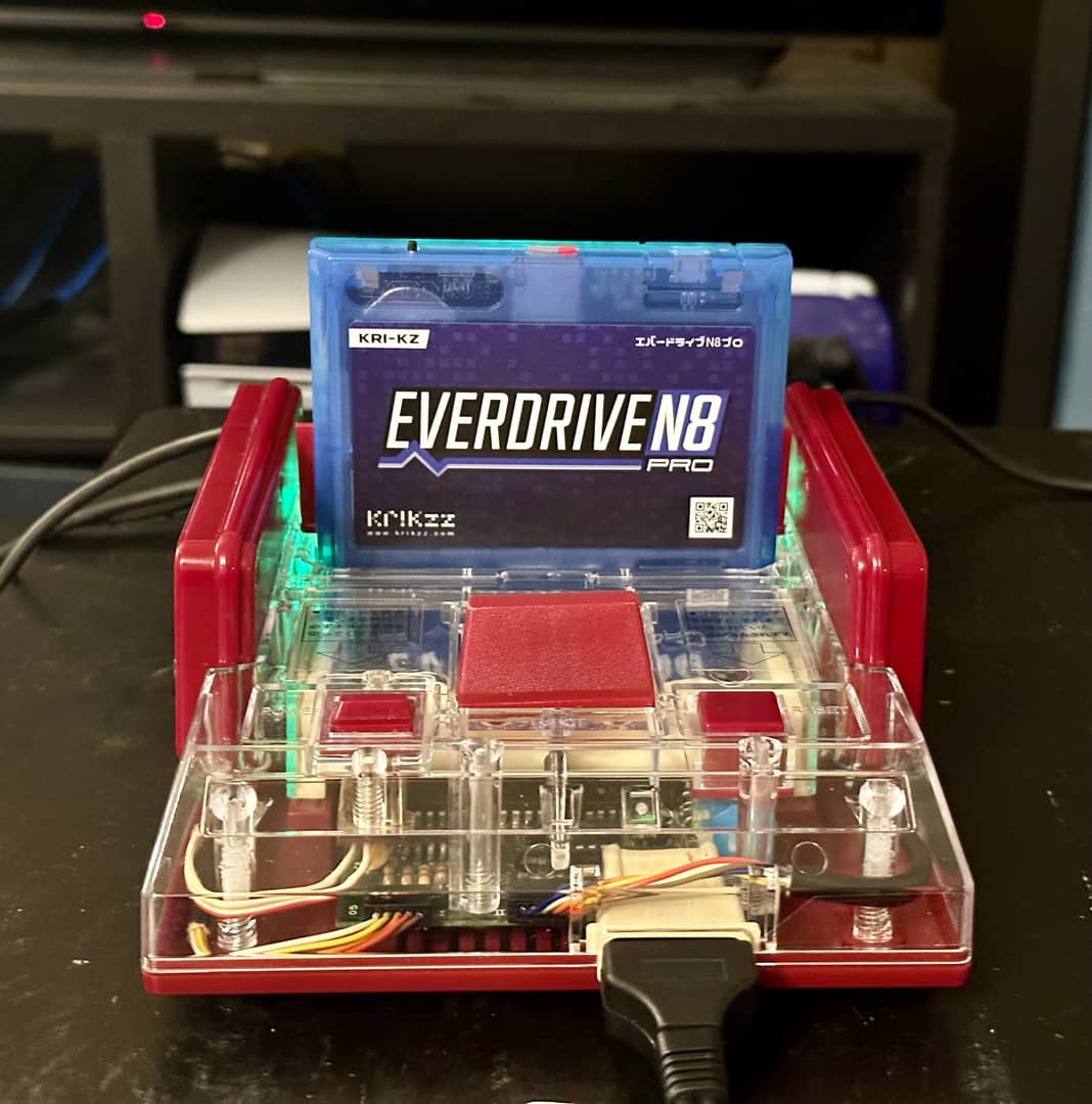 A Nintendo Famicom, with a transparent top. Inserted into it is a translucent blue Everdrive N8 Pro. A faint green light can be seen, coming from the rear of the Famicom.